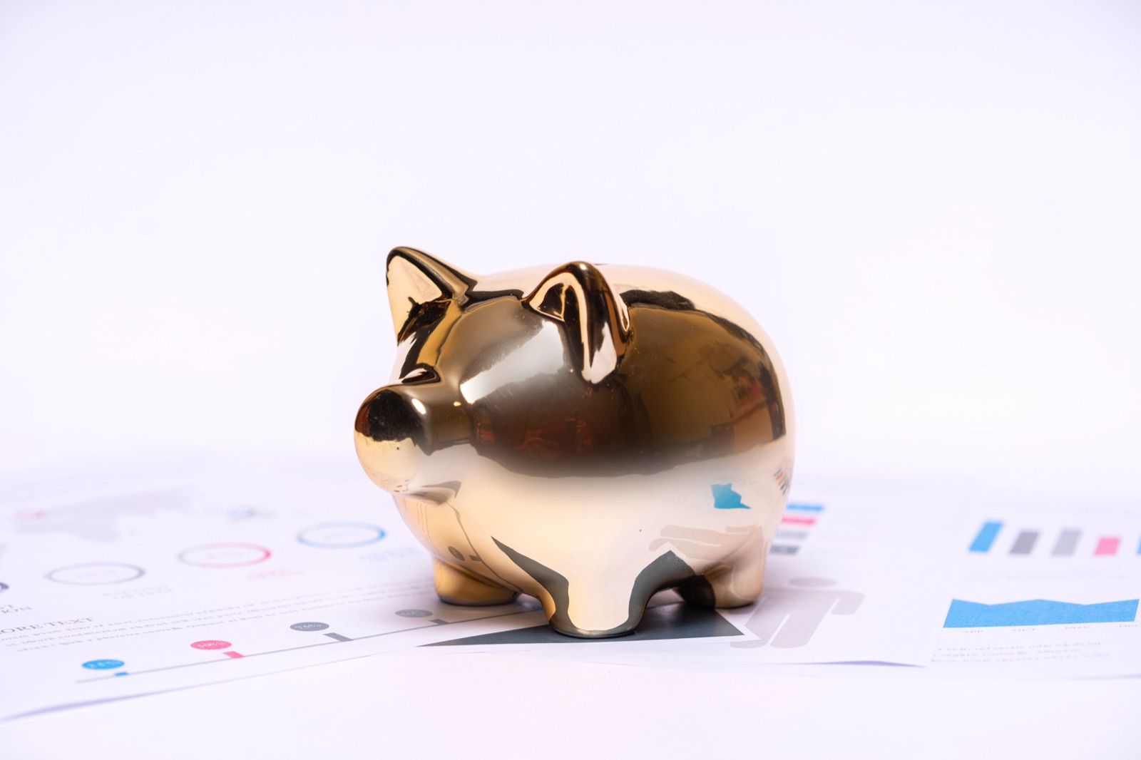 A gold piggy bank resting on printed financial charts