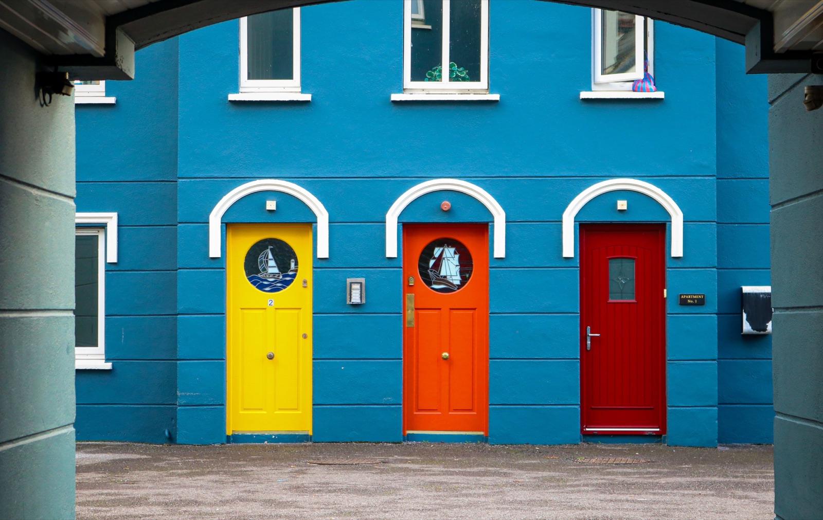 Three arched front doors painted yellow, orange and red on a blue building