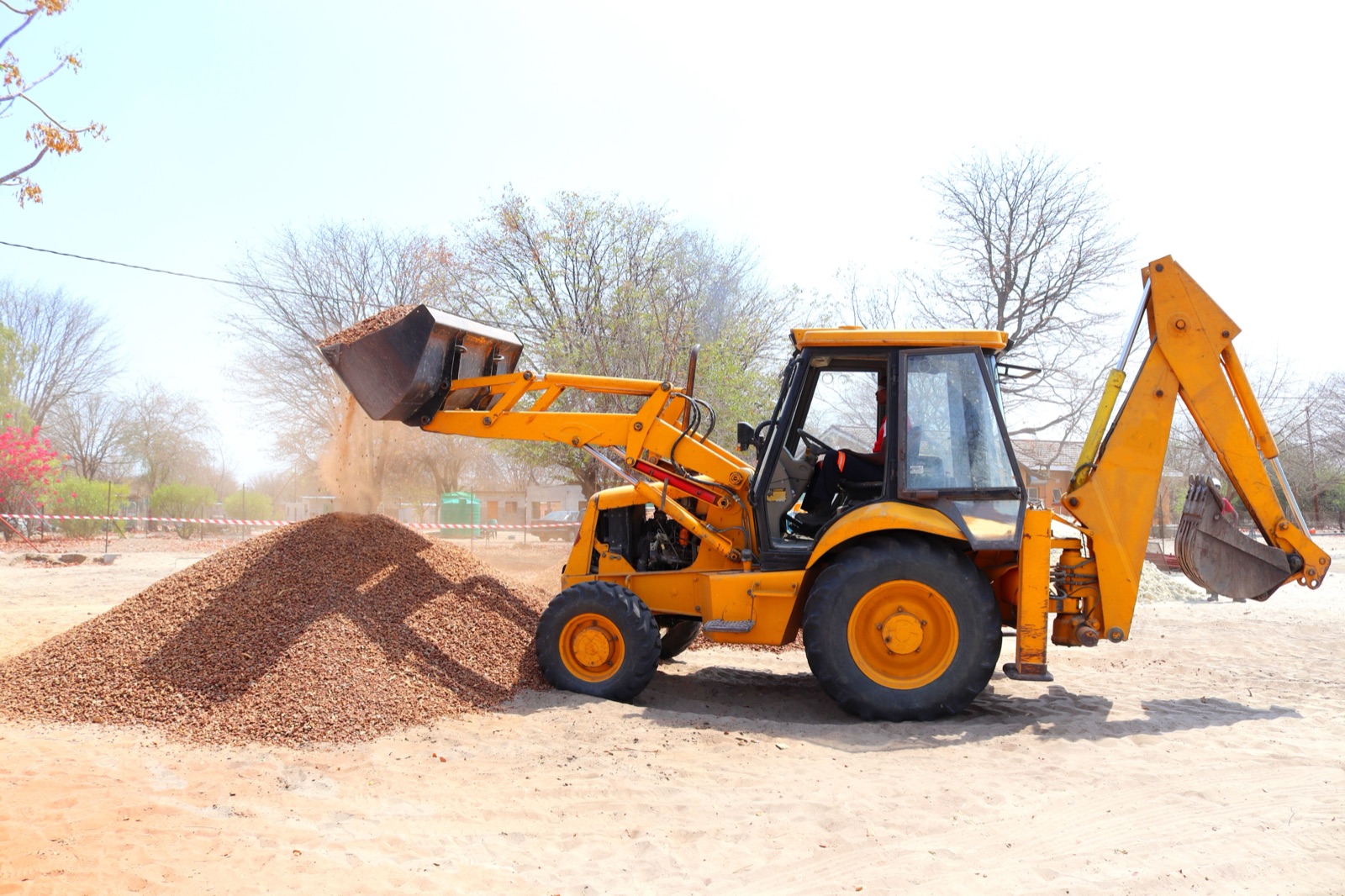 A yellow backhoe loader tipping gravel onto a pile at a work site