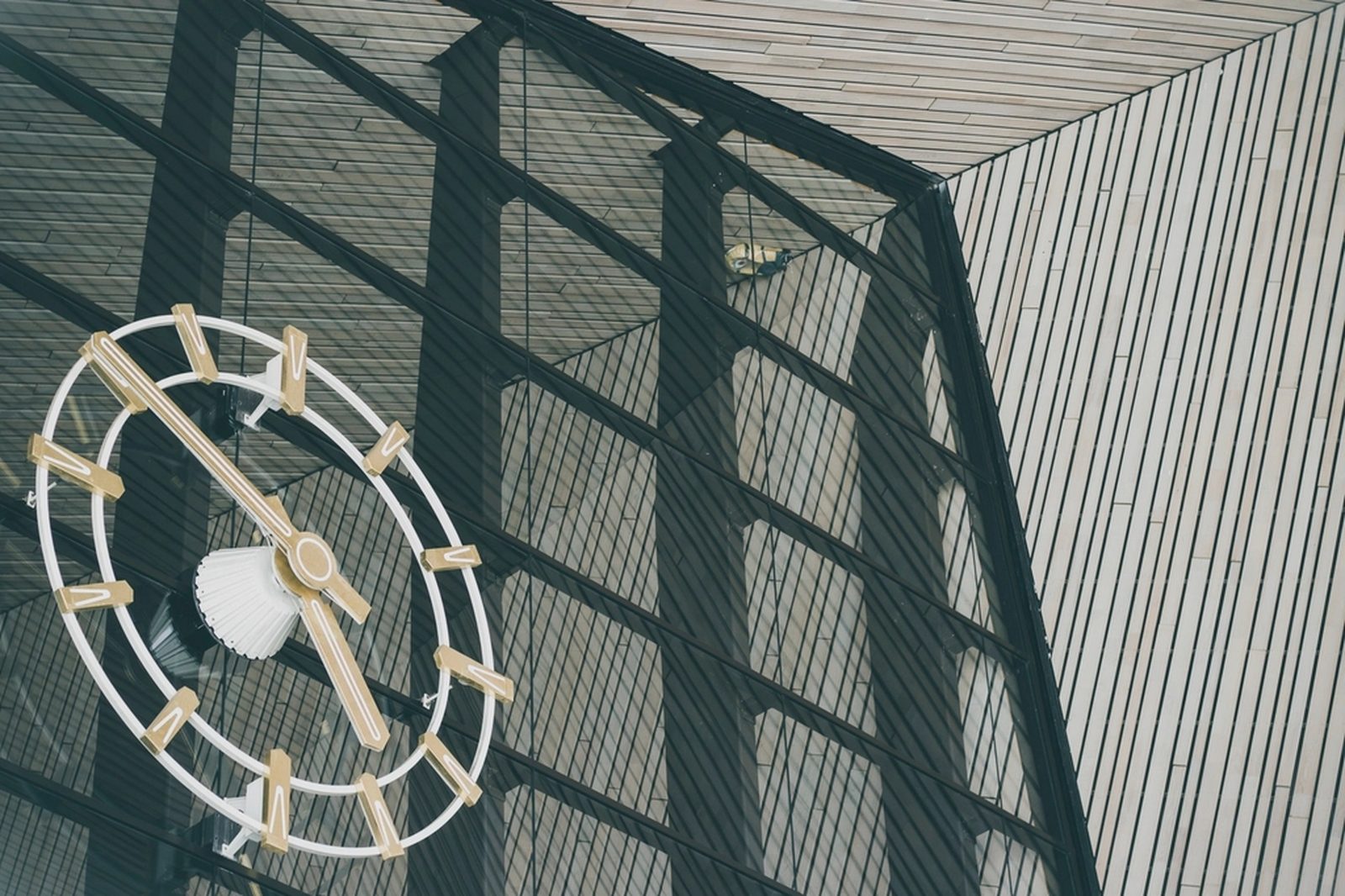 A large analog clock mounted on the glass and steel frame of a modern building