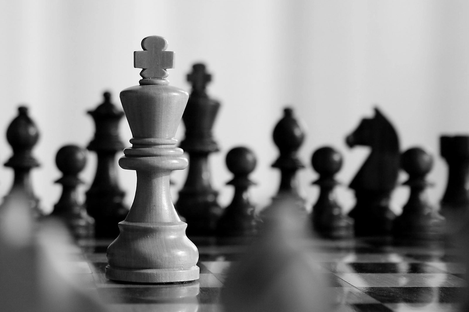 A white king chess piece in sharp focus in front of blurred black pieces